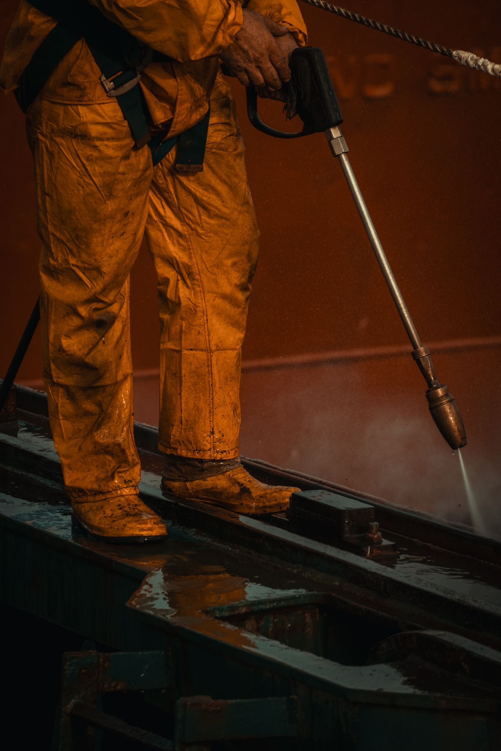 Technicien en équipement de sécurité décapant une machine au nettoyeur haute pression, chantier mené en local vide hors saison