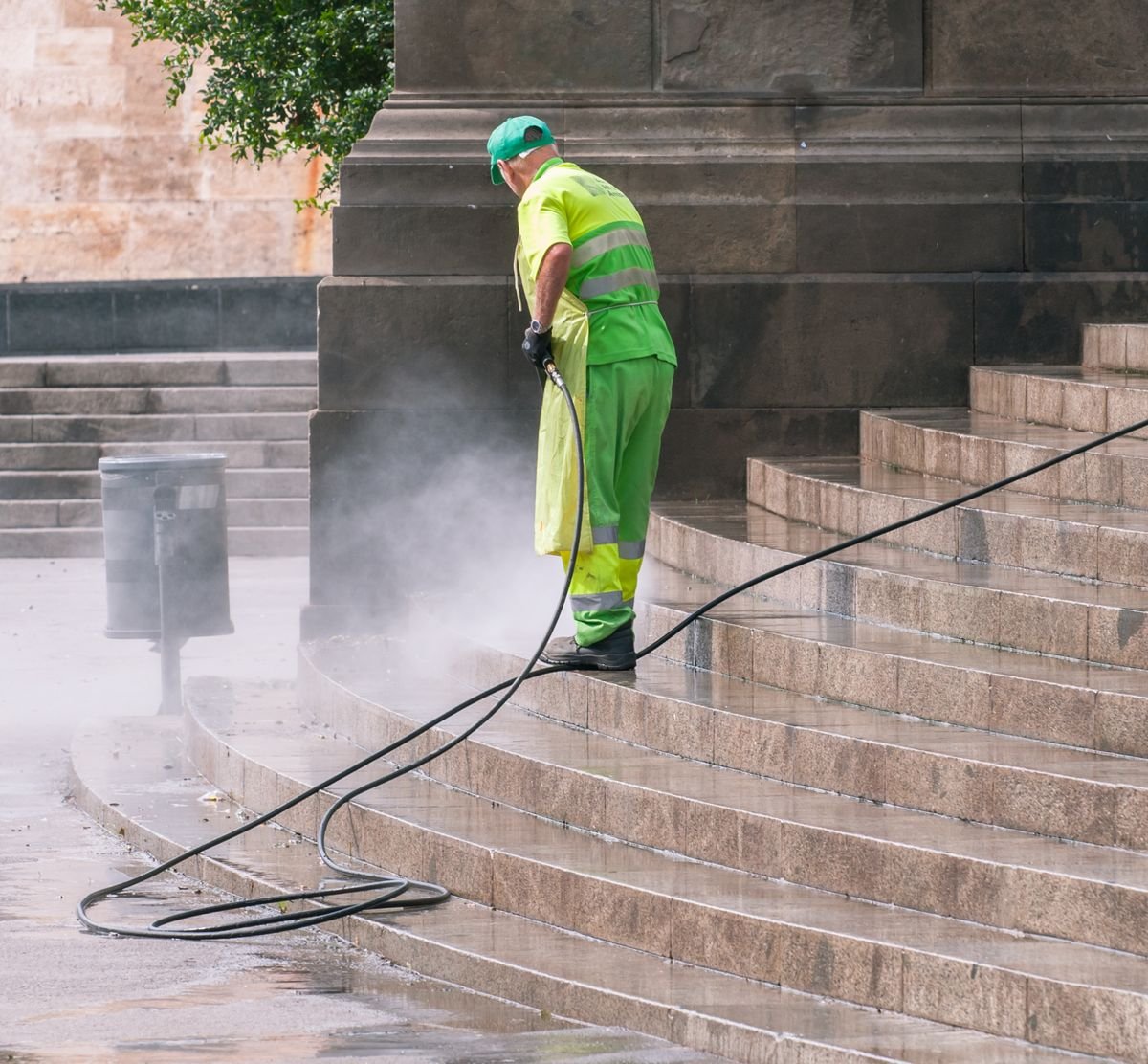 Opérateur en vêtement haute visibilité décapant un escalier de pierre au jet très haute pression, la vapeur d'eau au ras du sol