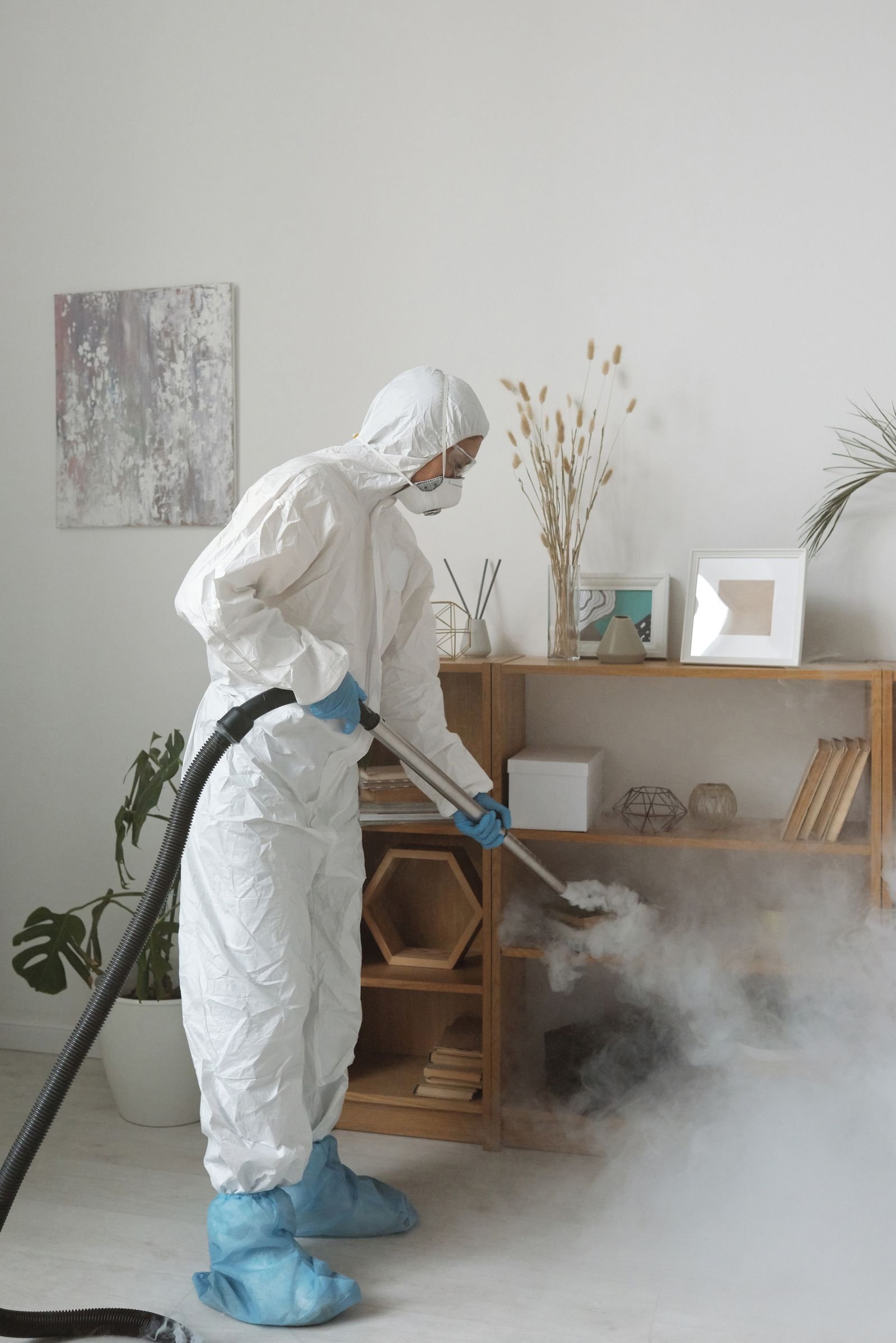 Opérateur en combinaison diffusant un brouillard désinfectant dans un volume fermé, technique employée là où la main n'atteint pas