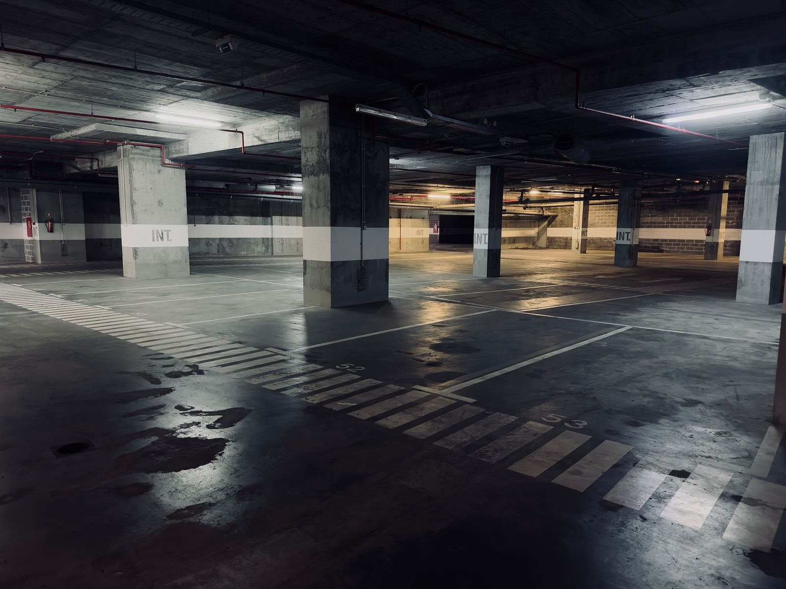 Niveau de parking souterrain désert avec des flaques stagnantes au sol, situation courante en copropriété toulonnaise après un orage d'automne
